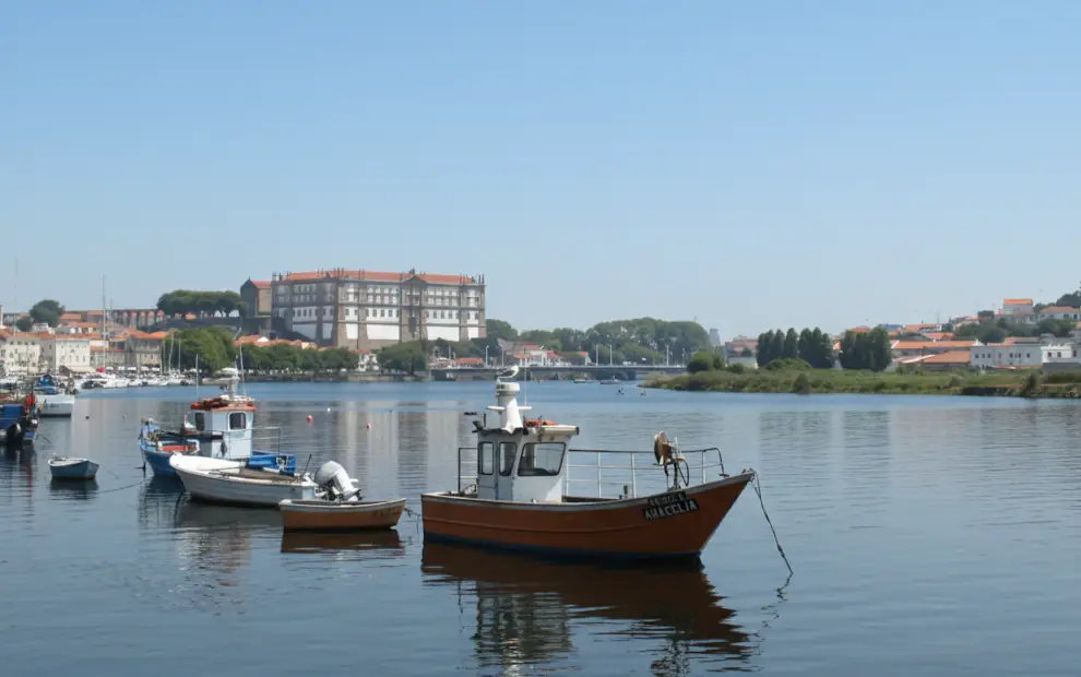 Blick über den Fluss Ave auf das Kloster Santa Clara und bunte Fischerboote in Vila do Conde am portugiesischen Jakobsweg